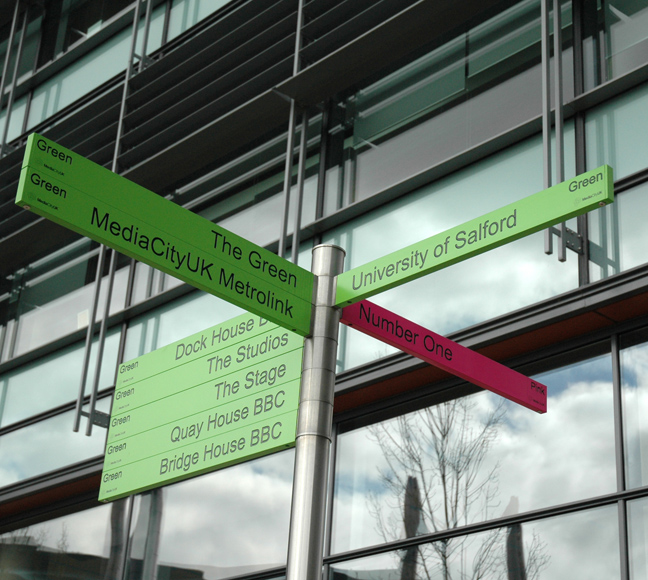 A green and pink signpost showing destinations at MediaCity