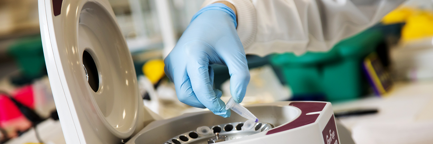 Gloved hands loading a blood card into the centrifuge in the Bodmer labs at the University of Salford