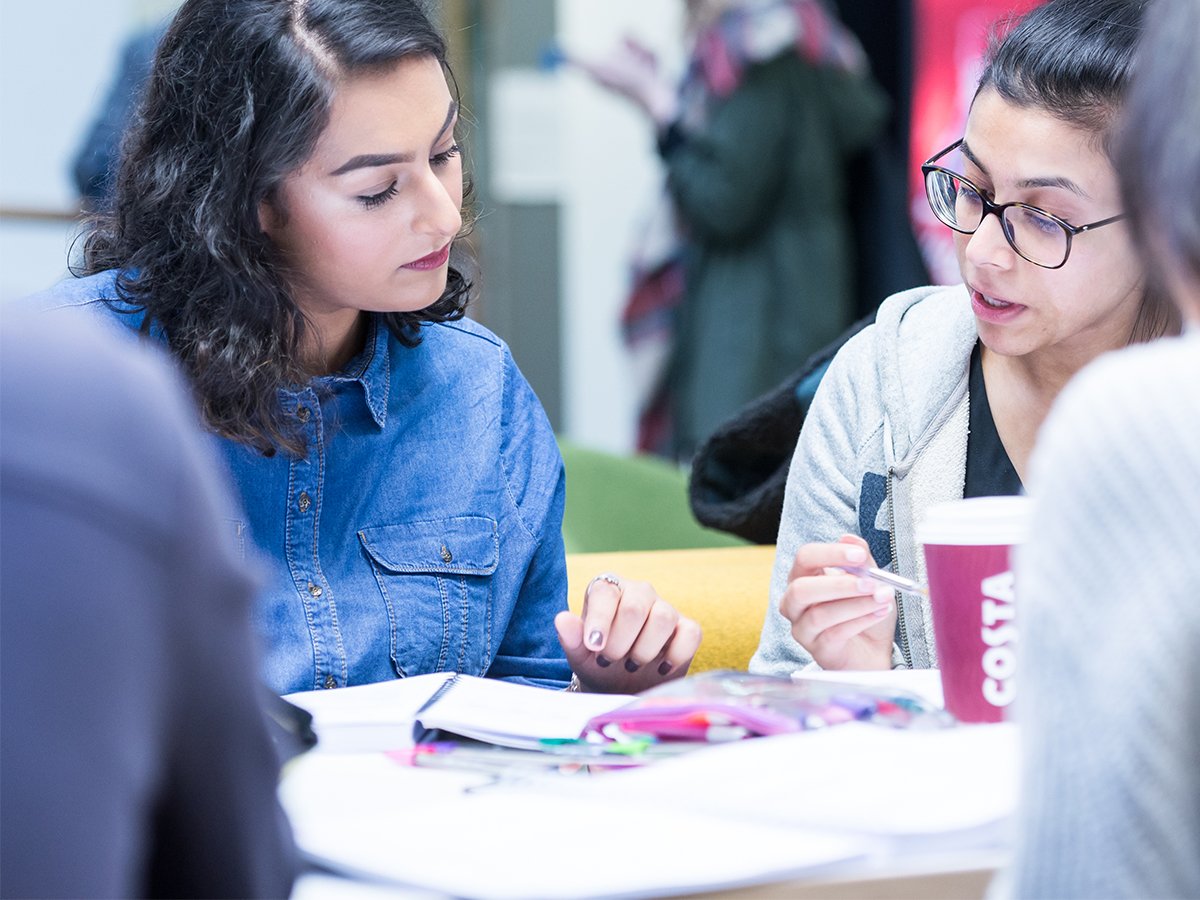 Two Salford students engaged in discussion, looking over notebooks during a seminar