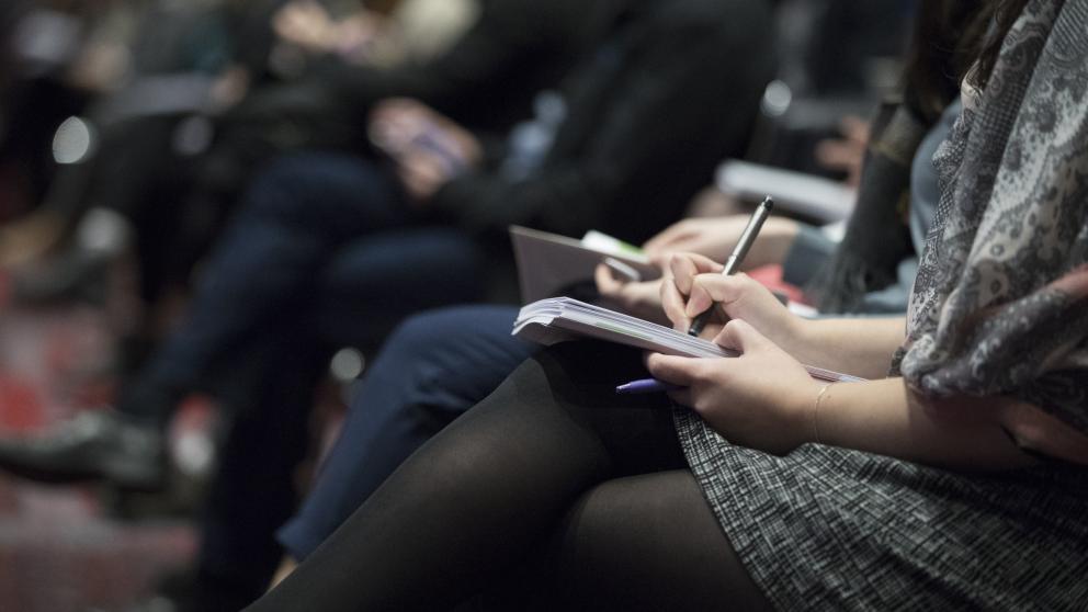 People writing in notepads at a conference