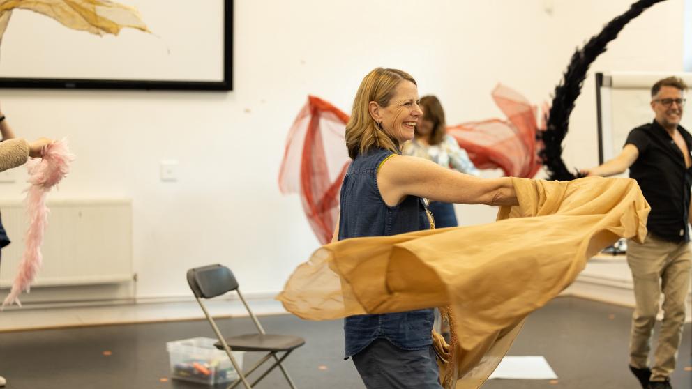 The image shows three people taking part in a workshop dancing and waving around colourful scarves