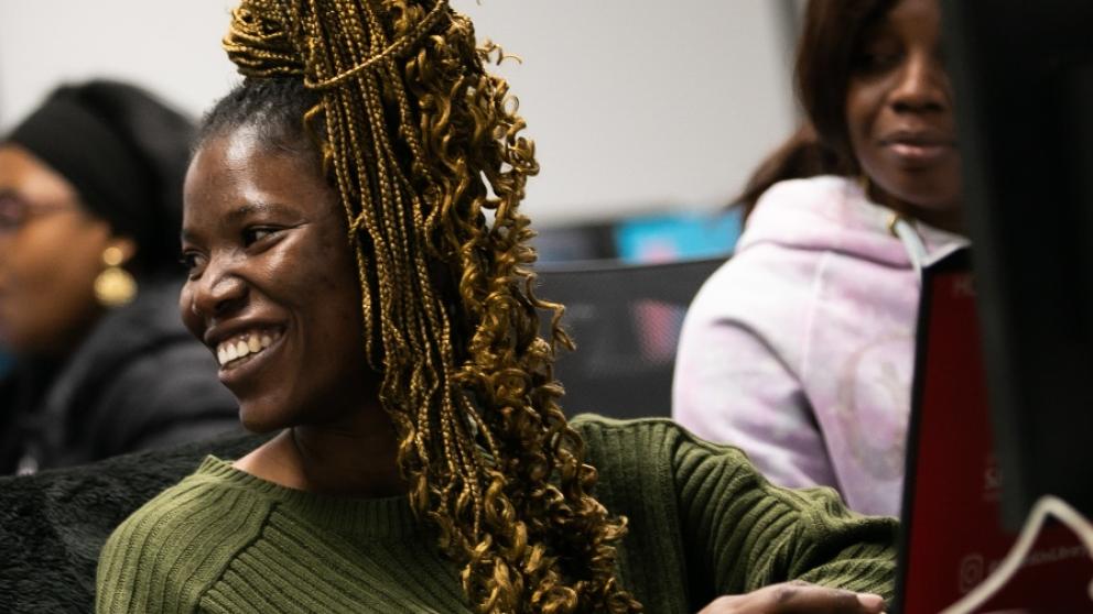 A female student smiling looking off camera in front of a desktop computer 
