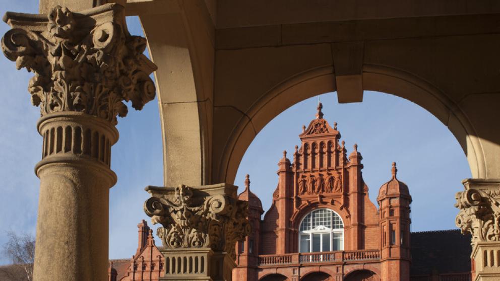 Top of Peel Building in the distance, a period terracotta brick building, as viewed through a stone archway
