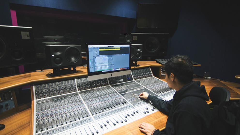 Salford music degree student sitting by high-tech recording equipment in the university’s recording studio facilities.