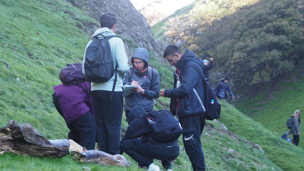 A group of Geography students studying something on the ground on the side of a hill during a field trip