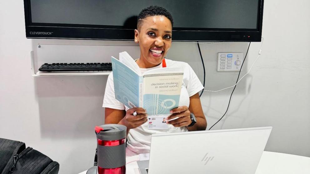 Student sat in a study room in front of a laptop holding an open text book