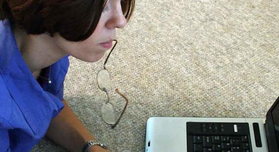 A student works on a laptop while holding their reading glasses in their mouth