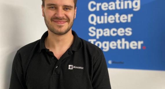KTP associate Gabriel Whittle stands in front of a sign that reads creating quieter spaces together