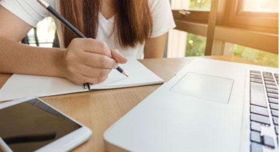 Student studying with a pen and paper at a laptop